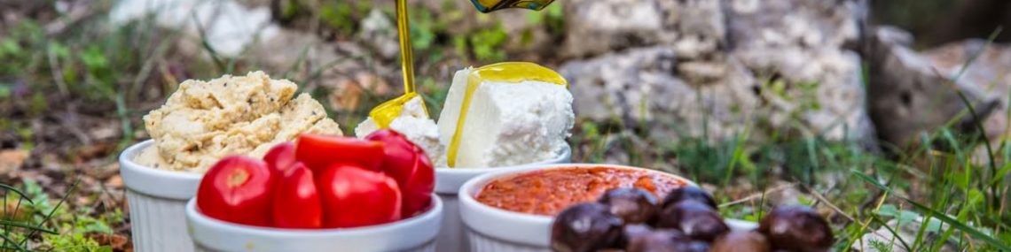 Outdoor picnic with various Mediterranean spreads, herbs, and olive oil drizzle.