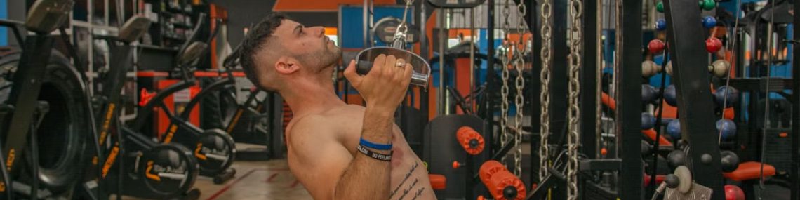 Tattooed man performs strength training on gym equipment, showcasing fitness.