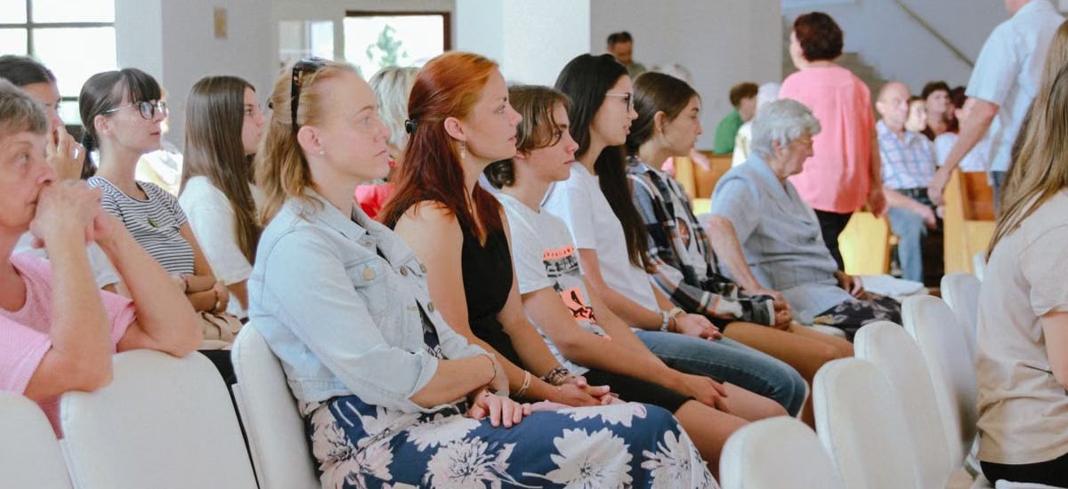 A diverse group of people sitting attentively during an indoor meeting or event, captured in a spacious room.